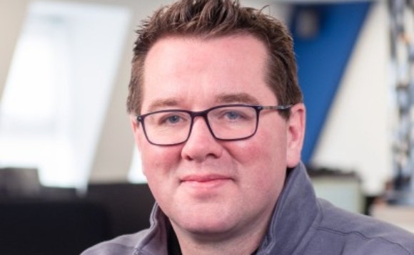 A person wearing glasses and a grey jacket Description automatically generated